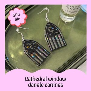 May include: Black dangle earrings with a stained glass window design. The earrings are made of resin and have a glittery finish.