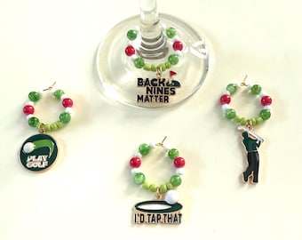 May include: Wine charms with green, red, and white beads. Charms include golf-themed pendants with text that reads "PLAY GOLF", "BACK NINES MATTER", and "I'D TAP THAT".