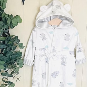 May include: White hooded bathrobe with a koala print and a tie belt. The robe has a gray and white striped lining in the hood.