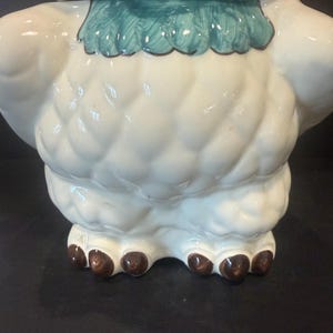 May include: A ceramic owl-shaped cookie jar. The jar is primarily white with textured detailing, a turquoise collar, and brown feet. The owl's head features red and brown accents.