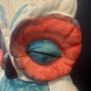 May include: A ceramic owl figurine with a glossy finish. The owl features a white body, red and teal accents, and a large, detailed eye. The eye is a vibrant teal color with a black slit pupil. The owl's design is whimsical and decorative.