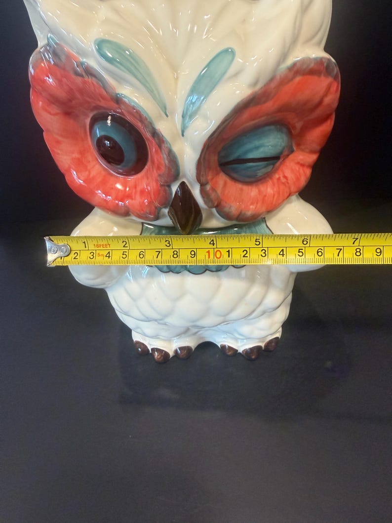 May include: A ceramic owl figurine with a white body, red and blue accents, and a brown beak. The owl's eyes are blue and red. The figurine is approximately 6 inches tall.