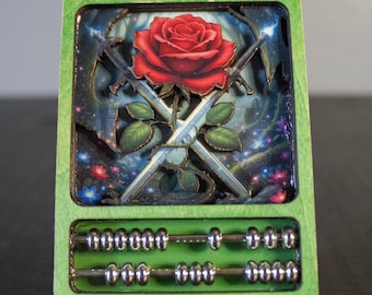 May include: A green wooden abacus with a detailed cutout design. The design features a red rose, crossed swords, and a starry background. The abacus has silver beads and a rectangular shape.