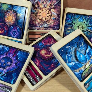 Puede incluir: Seis cajas de madera con diseños abstractos coloridos y características similares a un ábaco. Cada caja tiene una imagen diferente, incluyendo una calavera, un sol y un árbol.