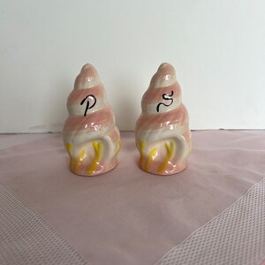 Peut inclure: Un ensemble de deux salières et poivrières en forme de coquillage rose et jaune. Les salières sont étiquetées "S" et "P" en noir.