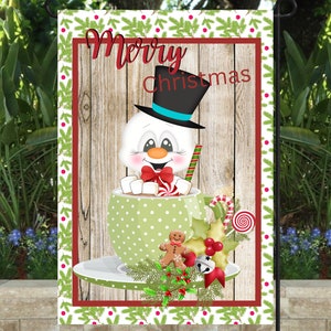 May include: A garden flag with a festive Christmas design. The flag features a snowman in a top hat, inside a green polka-dot mug of hot chocolate. The words "Merry Christmas" are written across the top. The flag is framed with a red border and a green and white pattern.