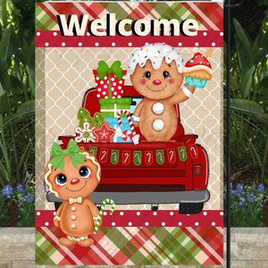 May include: A Christmas garden flag with the word "Welcome" at the top. The flag features a red truck filled with gifts and gingerbread people. The background has a tan pattern and a red and green plaid design.