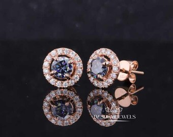 May include: A pair of rose gold stud earrings with a halo setting. The centre stone is a dark blue moissanite with a round cut. The halo is set with smaller round cut diamonds.