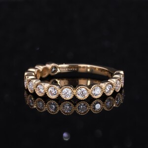 May include: A gold band ring with a row of bezel-set round diamonds. The diamonds are set in a scalloped design.