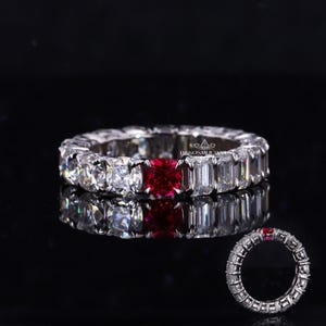 May include: A silver eternity band with a red square gemstone surrounded by smaller clear gemstones.