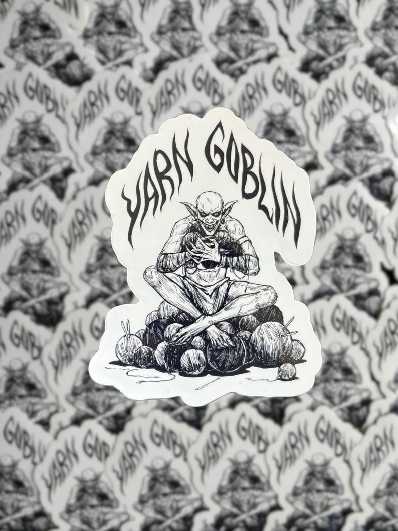May include: A black and white sticker featuring a goblin sitting on a pile of yarn balls. The goblin is holding a ball of yarn in its hands. The sticker reads "Yarn Goblin" in a stylised font.