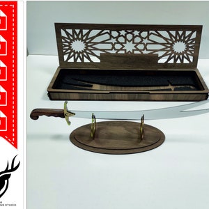 May include: A wooden box with an intricate laser cut design on the lid, open to reveal a sword on a stand. The sword has a silver blade and a gold handle. The box and stand are made of dark wood.