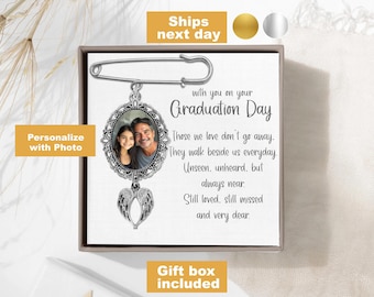 May include: A silver graduation day memorial pin with a photo frame and angel wings. The pin has the text "with you on your Graduation Day" and a quote about those we love don't go away. The pin comes in a gift box.