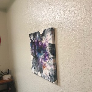 May include: Abstract painting on canvas with a white background and a large purple, blue, and orange flower-like design.
