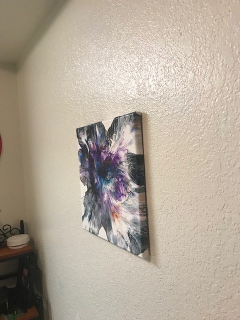 May include: Abstract painting on canvas with a white background and a large purple, blue, and orange flower-like design.