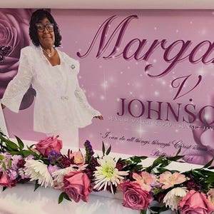 May include: A memorial display featuring a portrait of Margaret V. Johnson, with text including her name and dates. The background is pink with rose illustrations. A floral arrangement of pink and white flowers adorns the display.