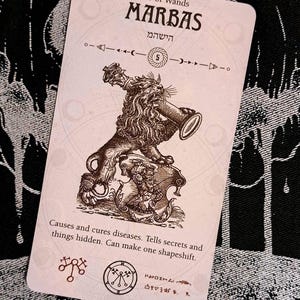 Puede incluir: Una carta de tarot con una criatura de león marrón que sostiene un bastón. La carta se titula "10 of Wands MARBAS" e incluye texto hebreo. La carta también incluye un sello y el texto "Causes and cures diseases. Tells secrets and things hidden. Can make one shapeshift."