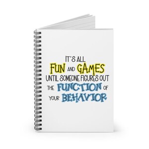 May include: A white spiral notebook with the text "It's all fun and games until someone figures out the function of your behavior" in black, yellow, and blue lettering.