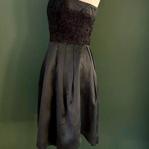 May include: A black strapless dress with a lace bodice and a pleated skirt. The dress is on a wooden mannequin.