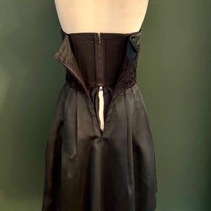May include: A black strapless dress with a fitted bodice and a full skirt. The dress has a zipper in the back and a lace trim at the top.