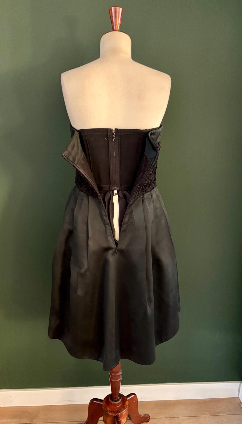 May include: A black strapless dress with a fitted bodice and a full skirt. The dress has a zipper in the back and a lace trim at the top.