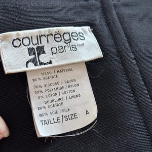 May include: White tag with black text reading "courr&egrave;ges paris" and fabric content information. The tag is attached to a black fabric garment. The fabric content information includes: "TISSU / MATERIAL 100% ACETATE 76% VISCOSE / RAYON 20% POLYAMIDE / NYLON 4% COTON / COTTON DOUBLURE / LINING 100% ACETATE 100% SOIE / SILK TAILLE / SIZE A"