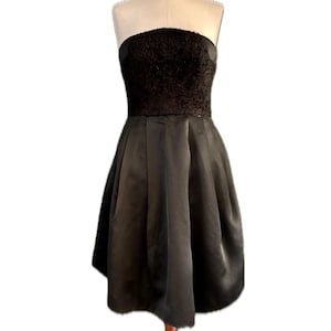 May include: A black strapless dress with a textured bodice and a flowing skirt. The dress is on a wooden mannequin.