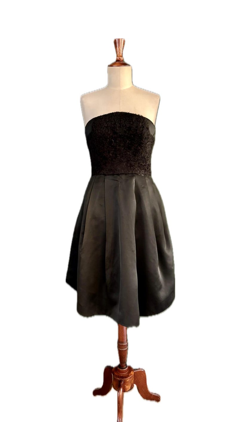 May include: A black strapless dress with a textured bodice and a flowing skirt. The dress is on a wooden mannequin.