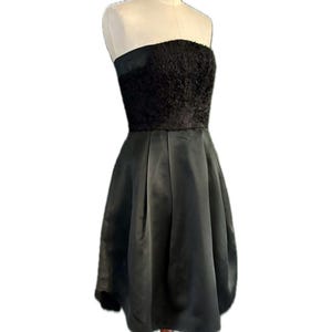 May include: A black strapless dress with a textured bodice and a flowing skirt. The dress is displayed on a wooden mannequin.