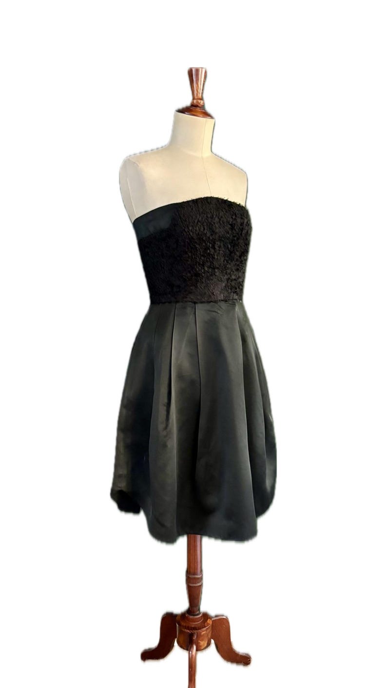 May include: A black strapless dress with a textured bodice and a flowing skirt. The dress is displayed on a wooden mannequin.