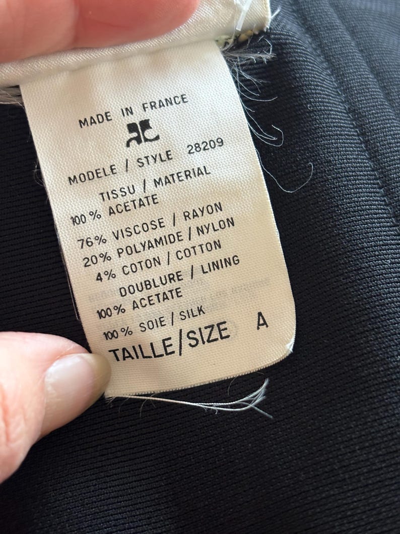 May include: White tag with black text detailing the fabric composition and size of a garment. The tag reads "Made in France", "Modele / Style 28209", "Tissu / Material", "100% Acetate", "76% Viscose / Rayon", "20% Polyamide / Nylon", "4% Coton / Cotton", "Doublure / Lining", "100% Acetate", "100% Soie / Silk", "Taille / Size A".