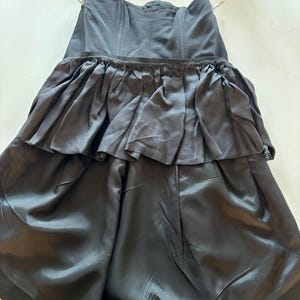 May include: A black strapless dress with a ruffled skirt. The dress is made of a smooth, silky fabric.