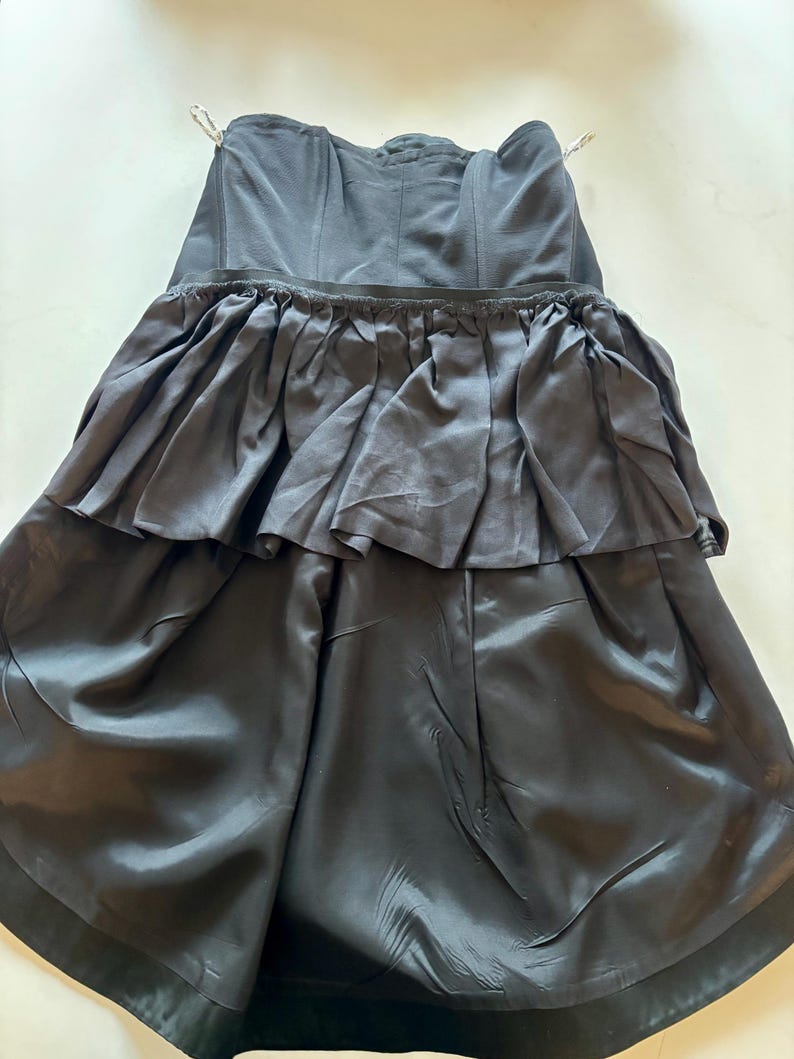 May include: A black strapless dress with a ruffled skirt. The dress is made of a smooth, silky fabric.