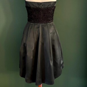 May include: A black strapless dress with a ruffled bodice and a full skirt. The dress is on a wooden dress form.