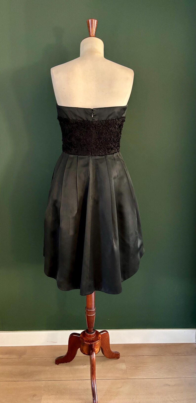 May include: A black strapless dress with a ruffled bodice and a full skirt. The dress is on a wooden dress form.