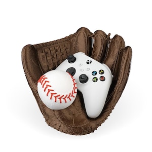 Op de afbeelding: Een witte videogamecontroller en een witte honkbal bevinden zich in een bruine leren honkbalhandschoen.