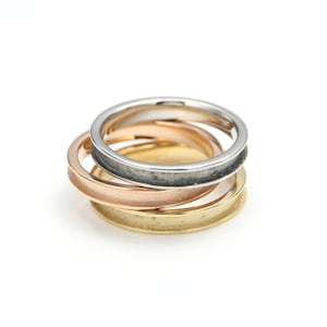 May include: Three stacked rings, one silver, one rose gold, and one gold. The rings are all thin and have a textured finish.