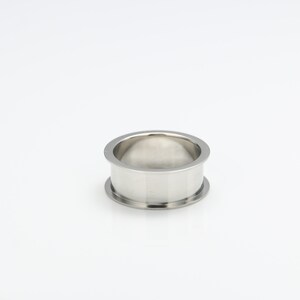 May include: A silver metal ring with a smooth, rounded surface. The ring is designed to be used as a spacer or connector for plumbing or other industrial applications.