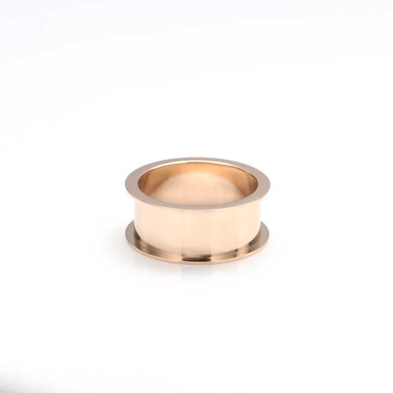 May include: A gold-colored metal ring with a wide band and a slightly rounded top.