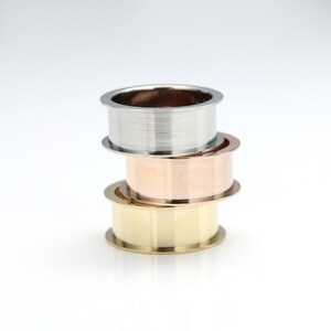 May include: Three stacked rings, one silver, one rose gold, and one gold. The rings are all smooth and have a polished finish.