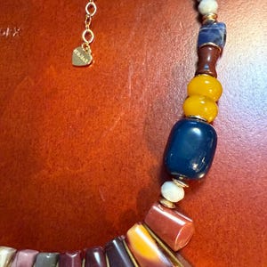 May include: A colorful necklace with a variety of beads in shades of yellow, blue, red, and purple. The necklace has a gold chain and a heart-shaped charm. The beads are various shapes and sizes.