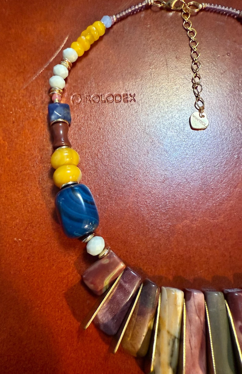 May include: A colorful necklace with a variety of beads in yellow, blue, brown, and white. The necklace has a gold chain and clasp. The text "ROLODEX" is visible on the background.
