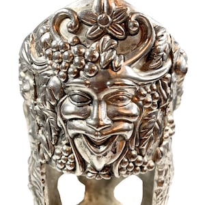 Peut inclure: Un bouchon de bouteille en argent avec un design détaillé d'un visage entouré de raisins et de feuilles.