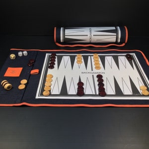 May include: A blue and orange backgammon set with a roll-up board, dice, and playing pieces. The board is laid out on a black surface.