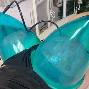 May include: Two blue plastic cups with clear water inside are attached to a person's body with black tubes. The cups are used for a beauty treatment.