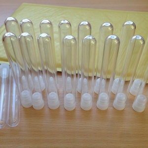 Puede incluir: Un conjunto de 20 tubos de plástico transparente con tapas blancas. Los tubos miden aproximadamente 10 cm de largo y 1 cm de diámetro. Los tubos están dispuestos en dos filas, con las tapas hacia arriba.