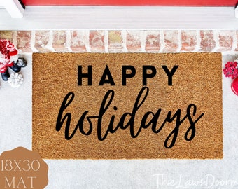 May include: A rectangular doormat made of natural coir fiber. The mat features the words "HAPPY holidays" in black lettering. The mat measures 18 x 30 inches. Festive holiday decor is visible in the background.