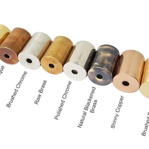 May include: A selection of cylindrical metal objects in finishes such as blackened brass, polished brass, and copper antique. Each cylinder has a central hole. Text labels identify each finish.