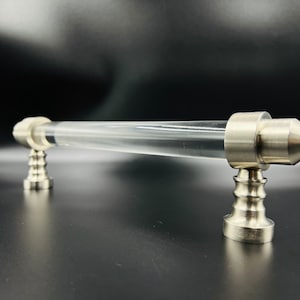 May include: A clear acrylic cabinet pull with silver metal end caps. The end caps have a pointed design.