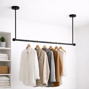 Peut inclure: Un portant noir suspendu au plafond, avec une barre horizontale, supportant des chemises sur des cintres en bois. Les chemises sont de couleurs neutres, dont blanc, beige, gris et marron. Le portant est suspendu par deux supports verticaux.